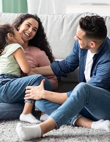 Familia sonriente sentada en la alfombra en un entorno familiar.