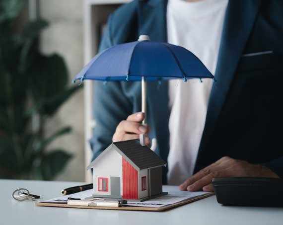 Maqueta representativa de una casa siendo resguardada por un paraguas dado una sensación de cuidado por el seguro.